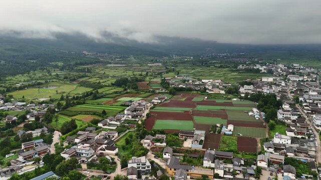 High angle aerial shot of Baisha ancient town and surrounding farmland under a cloudy sky in Lijiang, Yunnan. Perfect for travel documentaries and regional tourism videos.