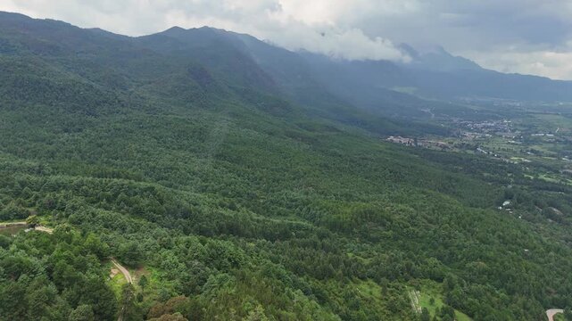 Panoramic drone footage showcasing the dense green forests and rolling hills surrounding Fuguo Monastery and Baisha town under a cloudy sky.
