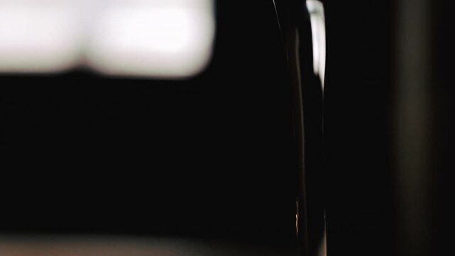 Close-up image of a stream of water flowing vertically against an undefined background of light and shadow.