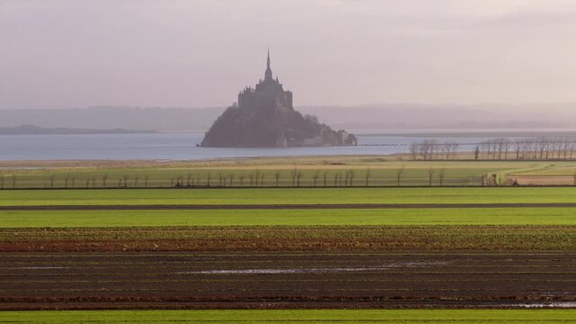 Aerial view of the historic Mont Saint-Michel abbey rising above the horizon with green agricultural fields in the foreground Mont Saint-Michel, Normandy, France.