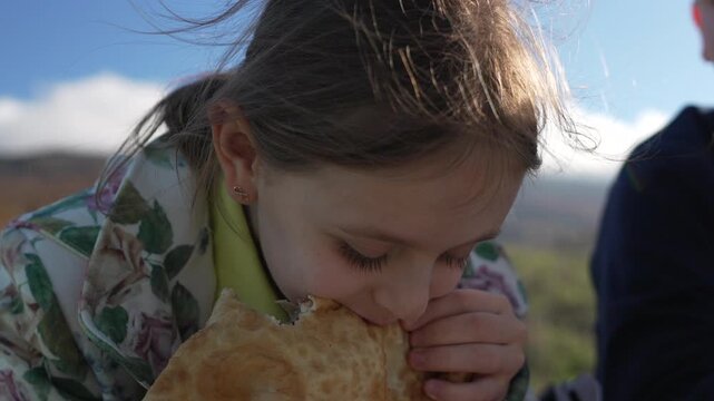 Child eating outdoors, hungry girl enjoying traditional flatbread during sunny mountain picnic lunch break
