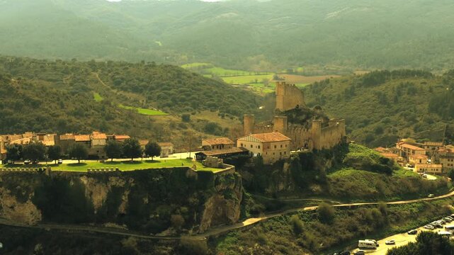 Vista a&eacute;rea cinematogr&aacute;fica del conjunto medieval de Fr&iacute;as, con etalonaje en tonos amarillos que aporta tensi&oacute;n y misterio. La arquitectura sobre la roca emerge entre sombras, evocando historia y sile