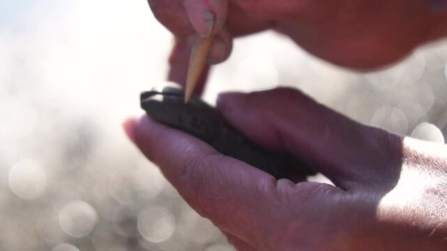 Clay crafting artist hands sculpting small intricate pattern detail on pottery outdoors in bright sunlight