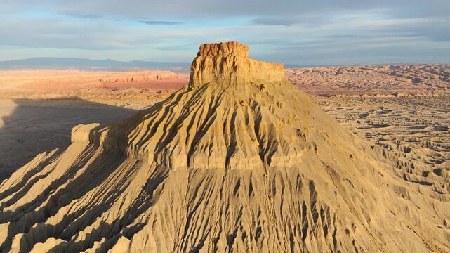 Aerial view of Factory Butte showing unique erosion patterns and desert badlands under a soft sky in Wayne County, Utah, United States.