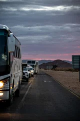 Bus And Cars On Desert Road, Headlights Cutting Through Moody Dusk Sky Long Slow Convoy Moves Along Remote © 21AERIALS