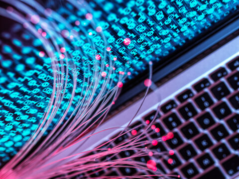 Fiber optic cables and binary code over laptop symbolize data transfer