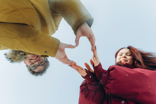 Couple making heart shape with hands outdoors in winter forest