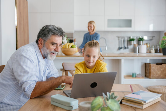 Grandfather and child learning together on laptop in kitchen