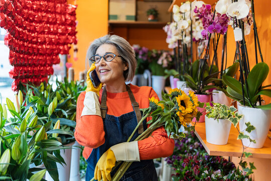 Florist working and talking on phone in flower shop holding sunflower