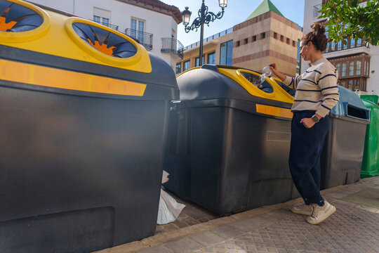 Woman recycling plastic bottle in yellow bin on sunny city street