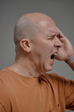 Bald man suffering from headache in studio with hand on head