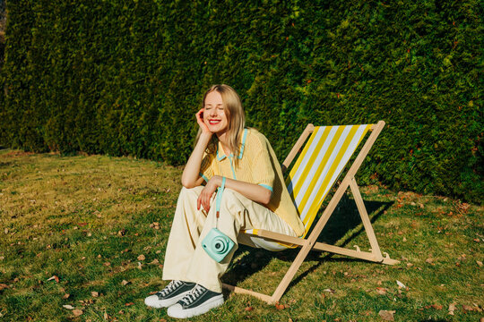 Woman relaxing with retro camera in striped garden chair outdoors