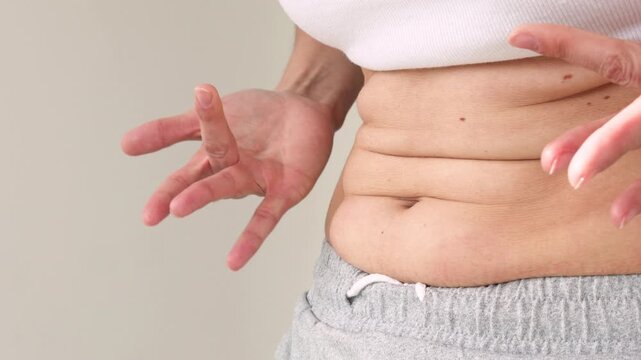 Close-Up of Woman's Hands Pinching Belly Fat Skin Fold at Waist in White Crop Top and Gray skirt &mdash; Female Checking Abdominal Subcutaneous Fat, Body Weight Awareness, Healthy Lifestyle Motivation