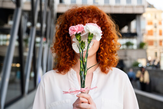 Redhead holding flowers covering face in urban outdoor setting