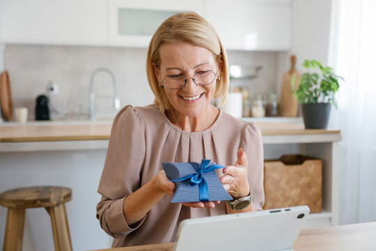 Smiling woman having video call indoors holding gift box
