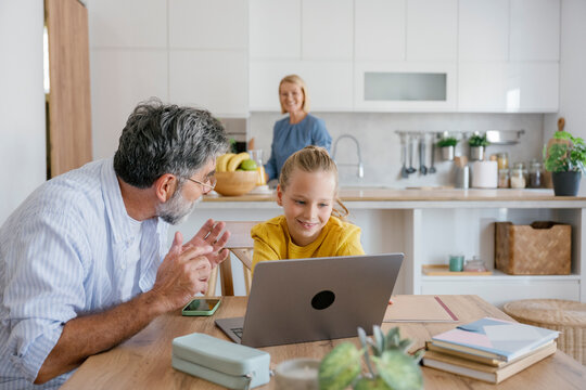 Grandfather and child using laptop at home with family in kitchen