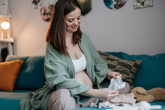 Pregnant woman joyfully preparing baby clothing at home