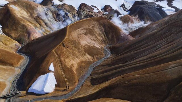 Aerial view of Kerlingarfjoll rhyolite mountains with steam vents, snow patches and people walking on hiking trails in Kerlingarfjoll, Hrunamannahreppur, Iceland.