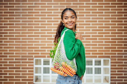 Smiling woman with mesh bag of vegetables embracing zero waste lifestyle