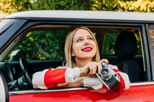 Smiling stylish woman with vintage camera in retro car looking up outdoors