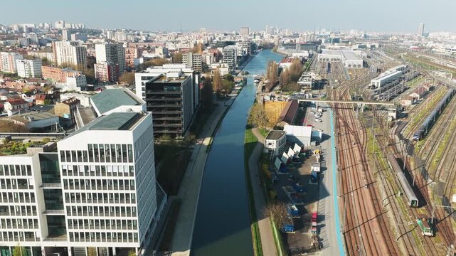 Aerial view of the Canal de l'Ourcq with its calm waters running through the urban landscape amid buildings and railway tracks, Bobigny, Ile-de-France, France.