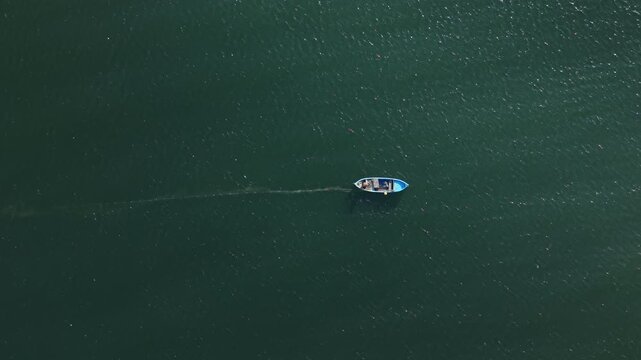 A small boat is traveling across dark water. It leaves a light trail behind. The surroundings are calm and open. The scene shows the boat in the middle of water.