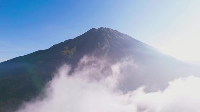 Aerial view of Mount Sumbing's majestic peak piercing through ethereal clouds, its slopes a tapestry of verdant forest, Nepal van Java, Mount Sumbing, Indonesia.