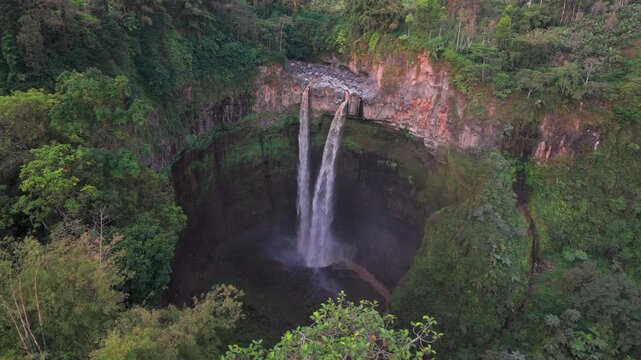 Aerial view of cascading waterfalls plunging down rocky cliffs amidst dense, lush green vegetation, Coban Sitri, East Java, Indonesia.