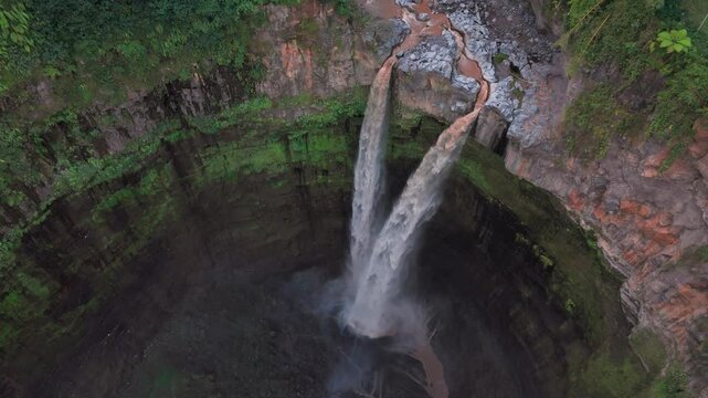 Aerial view of a majestic waterfall cascading down rugged cliffs surrounded by verdant greenery, creating a stunning contrast, Coban Sitri, East Java, Indonesia.