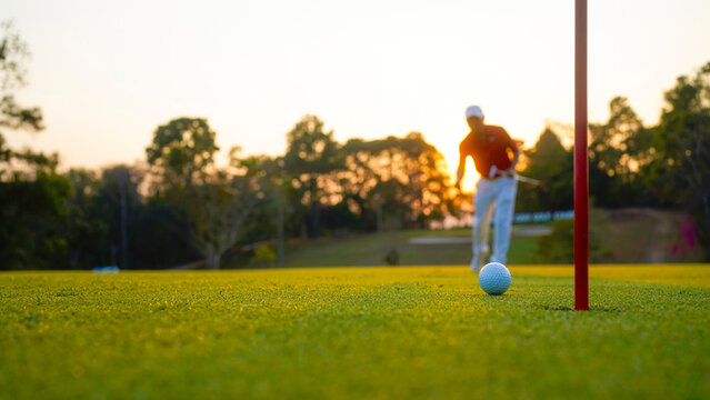 Golfer putting ball on the green golf, lens flare on sun set evening time.