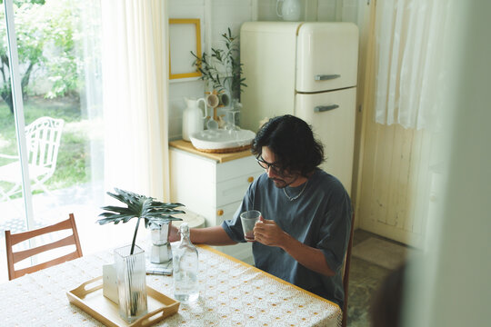 Relaxed bearded Japanese man in glasses enjoying a holiday coffee at home.