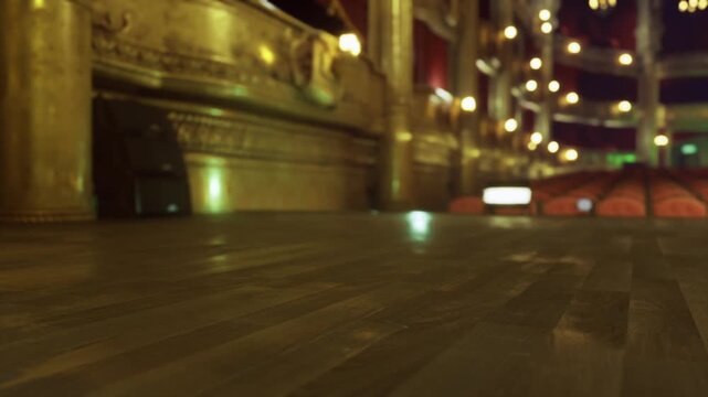 Close lowangle wooden floor with blurred lights, foreground texture of aged planks, subtle reflections of warm bulbs, background hint of actor prop case and red