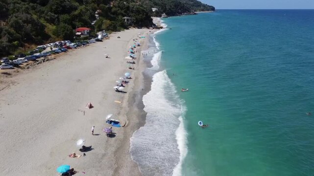 Cinematic drone push-in shot over Papa Nero beach in Pelion. High-angle view of the golden sand, colorful umbrellas and crystal clear Aegean sea. Ideal for travel and tourism storytelling.