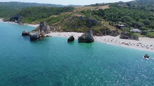 Cinematic drone orbit shot of the iconic giant rocks at Potistika beach. High-angle view of turquoise Aegean waters, golden sand and lush green hills in Pelion. Ideal for travel and tourism promos.