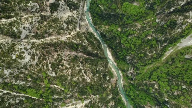 Cinematic top-down drone shot of the deep Acheron river gorge in Epirus. High-angle view of the turquoise water flowing between steep rocky cliffs and lush green forest. Stunning natural contrast.