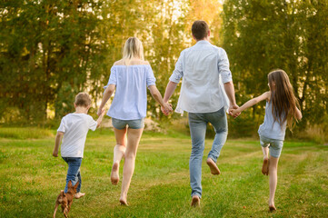 Obraz premium Happy Family Running Barefoot on Green Grass in Summer Park, Back View of Parents and Children Holding Hands. Freedom and Togetherness Concept, Rural Vacation, Leisure Time, summer holidays