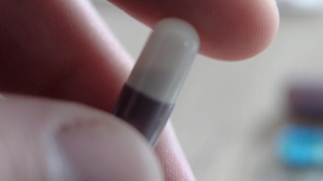 Close up of person's fingers holding a pharmaceutical capsule with two tone colors