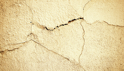 Obraz premium Dilapidated stone wall with deep cracks and peeling stucco. Warm sepia tones and vignette filter processing