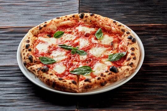 Fresh Neapolitan Margherita pizza with melting mozzarella, tomato sauce, and basil leaves on a dark wooden background.