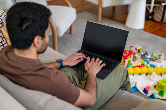 Indian man sitting on the couch in the living room working on his laptop
