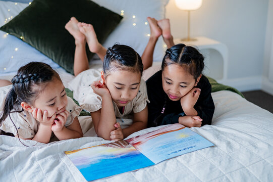 Young kids lying on their belly on the bed reading a colourful storybook