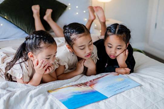 Young kids lying on their belly on the bed reading a colourful storybook