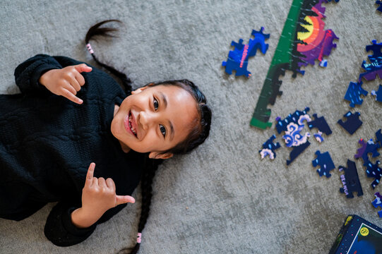 Young Samoan boy lying on the floor surrounded by scattered puzzle pieces doing cool guy hand sign