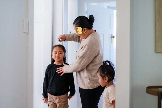 Young Samoan boy with braided hair standing against the wall while mum measures his height