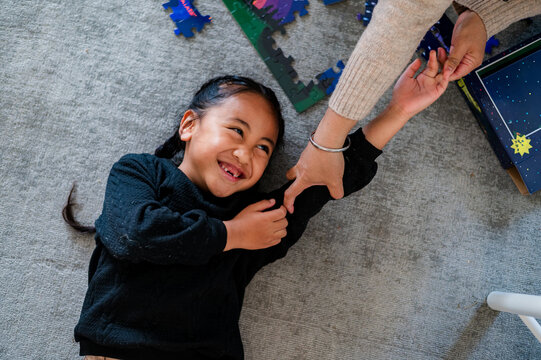 Young Samoan boy lying on the floor surrounded by scattered puzzle pieces tickled by adult hand