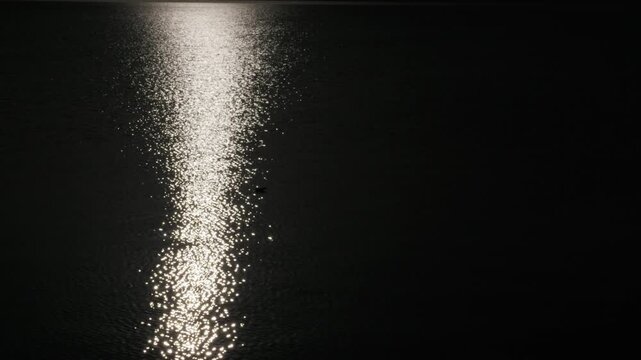 Bright moonlight reflects and sparkles across the gently rippling surface of dark water. The concept represents mystery, tranquility, and the quiet passage of time in nature.