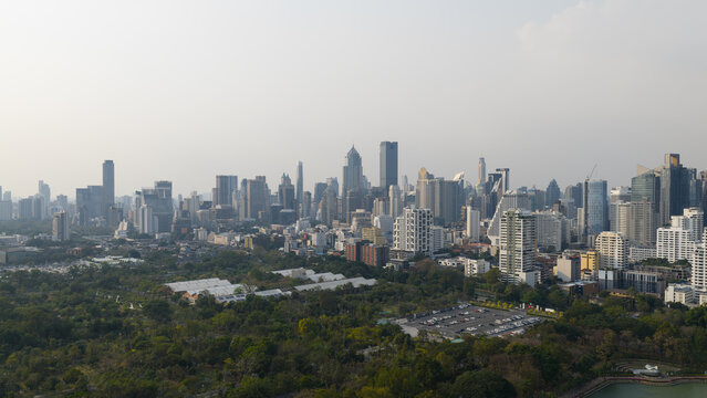 Bangkok, Thailand - 05 February 2026: Aerial view of Benjakitti Forest Park with its lush green trees and the modern city skyline of skyscrapers under a hazy sky.