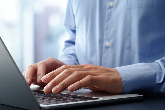 Businessman using laptop computer at desk in office. Closeup of hands and keyboard. Business technologies.