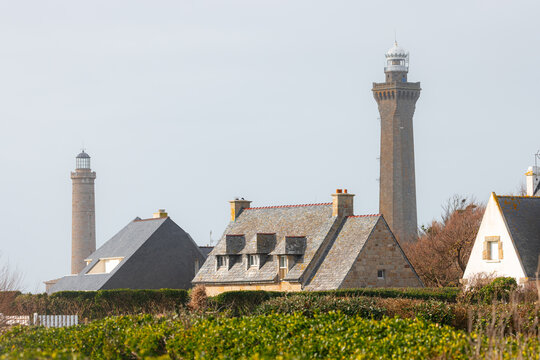 View of the Phare d'Eckmuhl lighthouse and traditional stone houses with slate roofs under a clear sky in Penmarch, Bretagne, France.