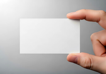 Obraz premium A close up view of a person holding a blank white business card against a soft grey background for professional branding design